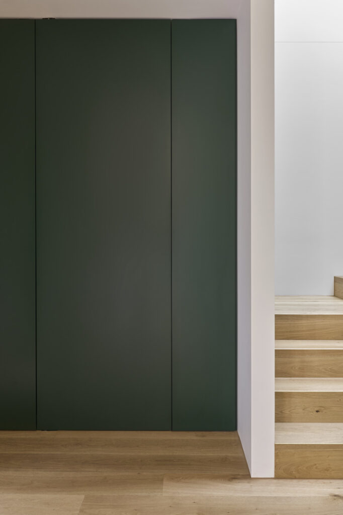 Concealed dark green door integrated within timber-lined hallway.
