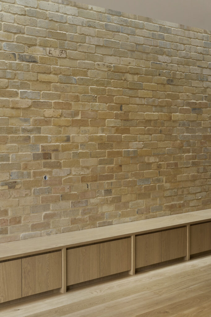 Low oak joinery set against reused internal brick feature wall in Fitzroy Passivhaus living space.