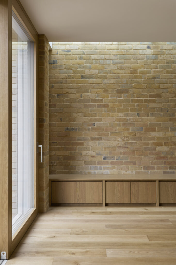 Built-in oak bench set against retained internal brick wall in Fitzroy Passivhaus.